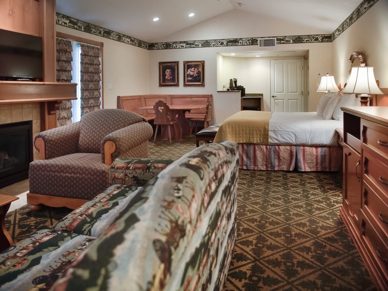Ein Hotelzimmer mit einem gemusterten Teppich, einer Couch, einem Sessel, einem Bett, einem Schminktisch und einem Fernseher.