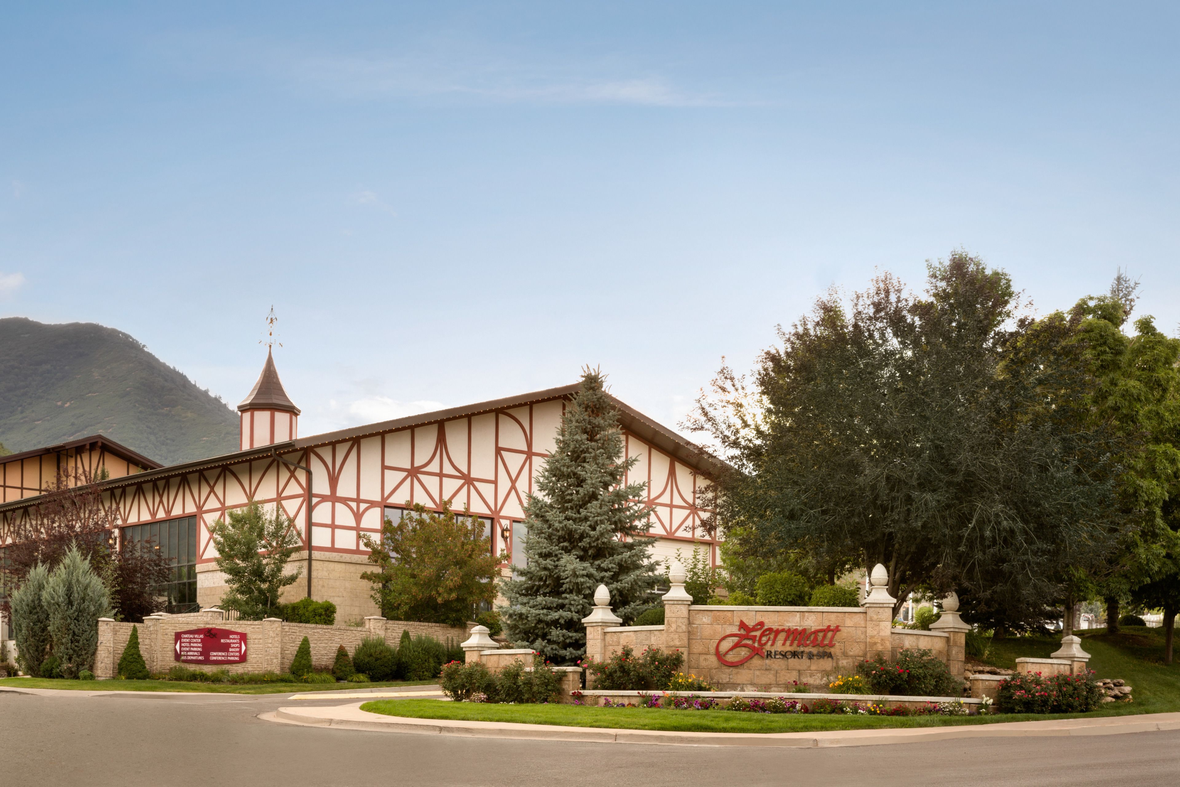 A hotel with a Tudor-style facade, a prominent tower, and a well-maintained garden with various plants and a signboard.