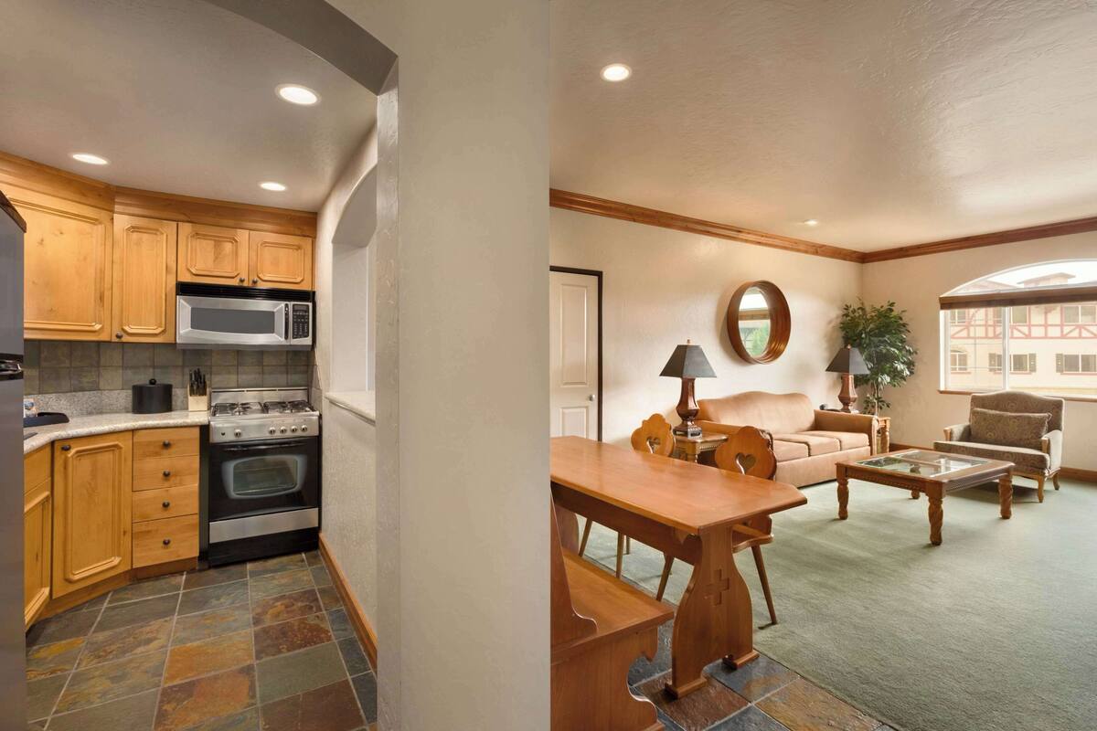 A kitchen with wooden cabinets, a stove, and a microwave. There is a dining area with a table, chairs, and a sofa.