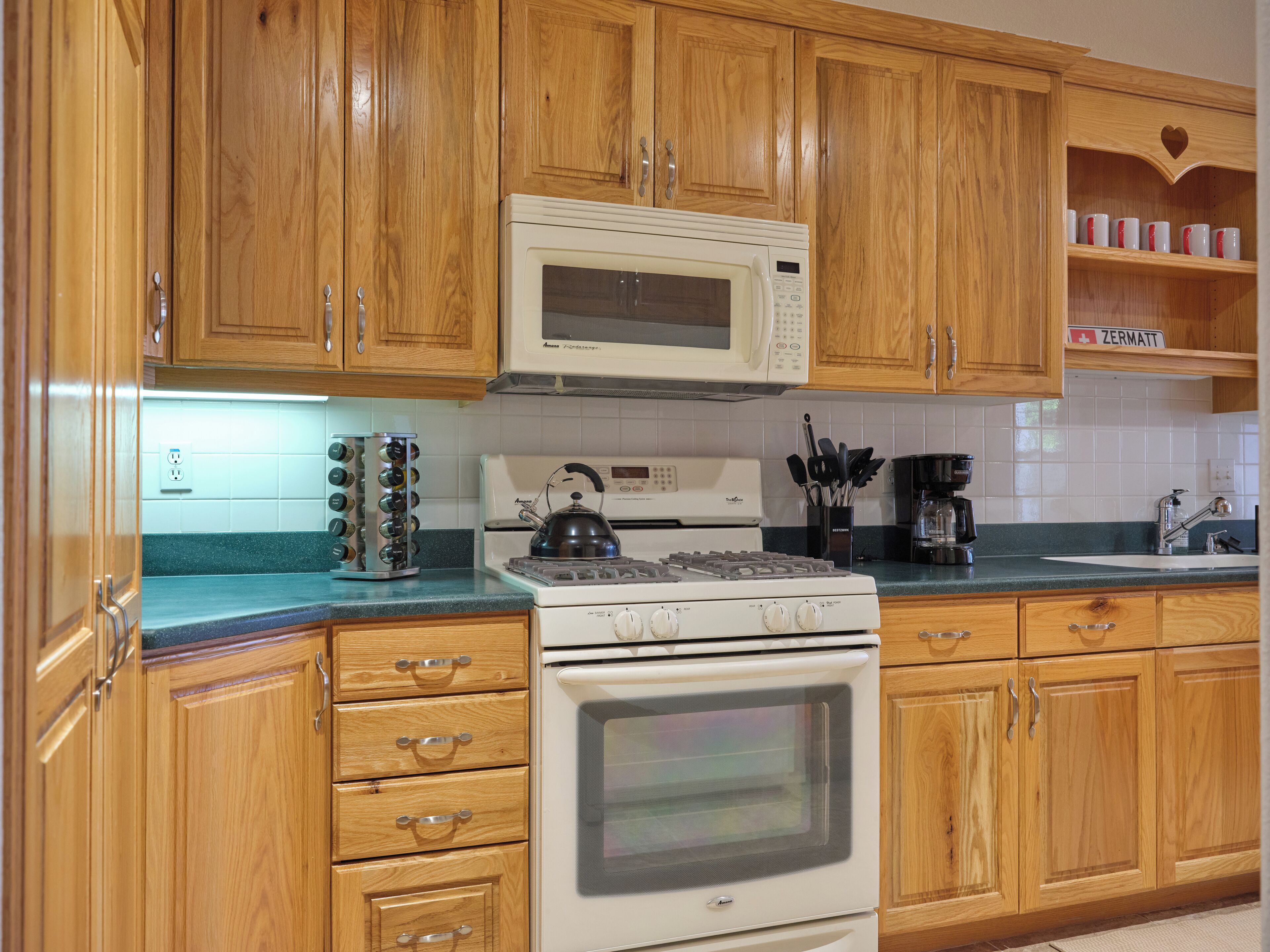 A kitchen with wooden cabinets, a white stove, a microwave, and a kettle.