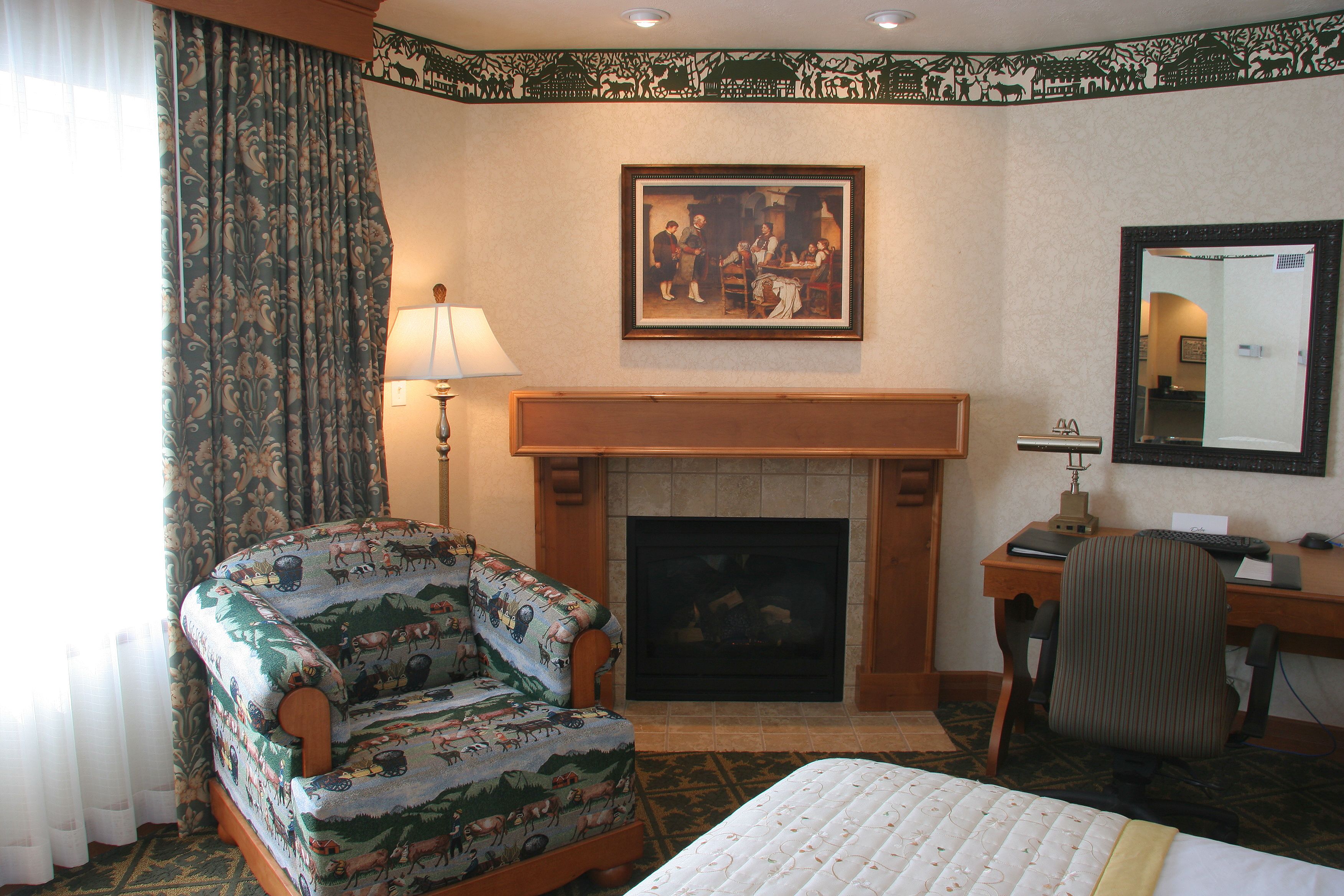A hotel room with a bed, a chair, a desk, a fireplace, and a painting on the wall.