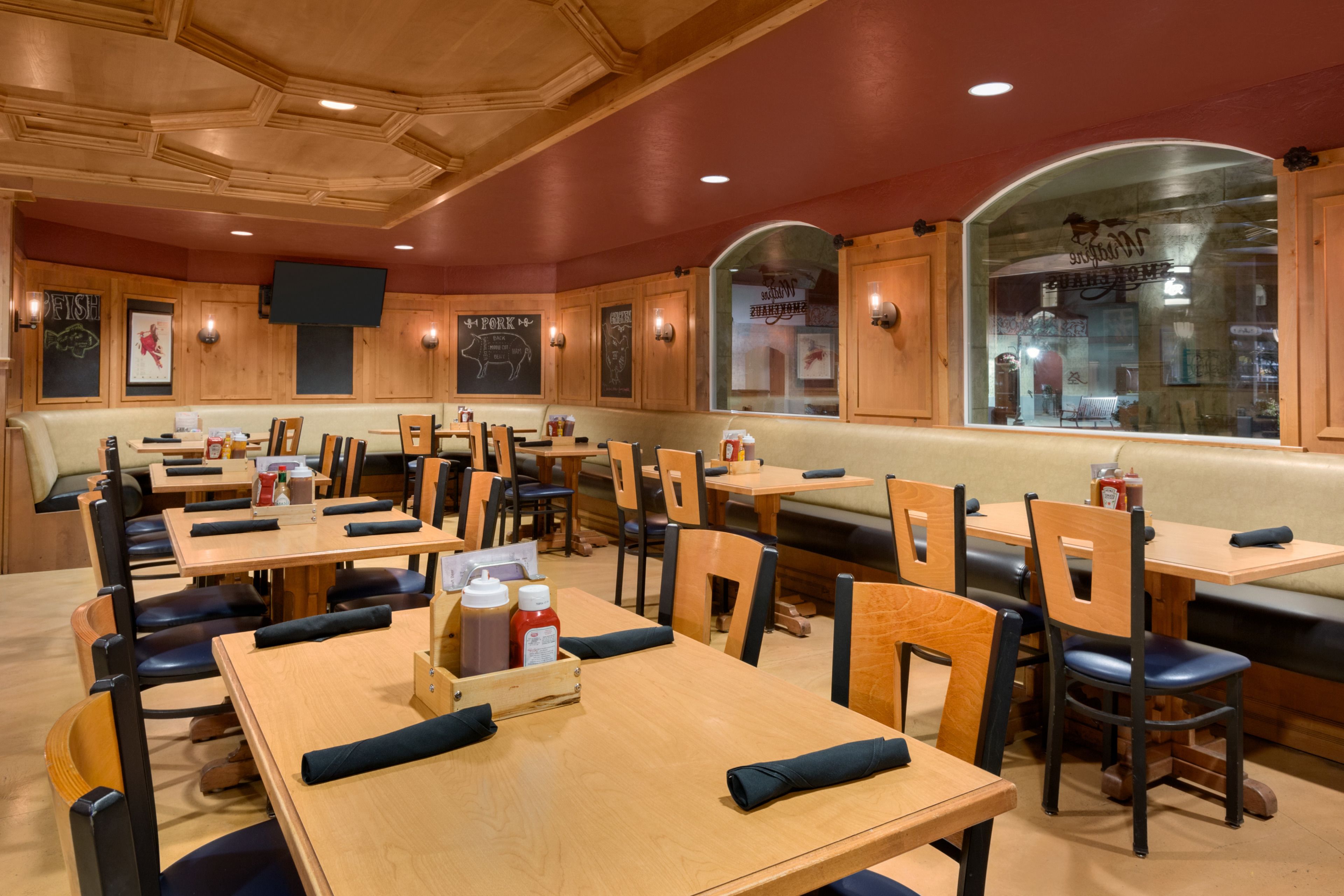 A restaurant interior with wooden tables and chairs, a large window, and wall-mounted televisions.