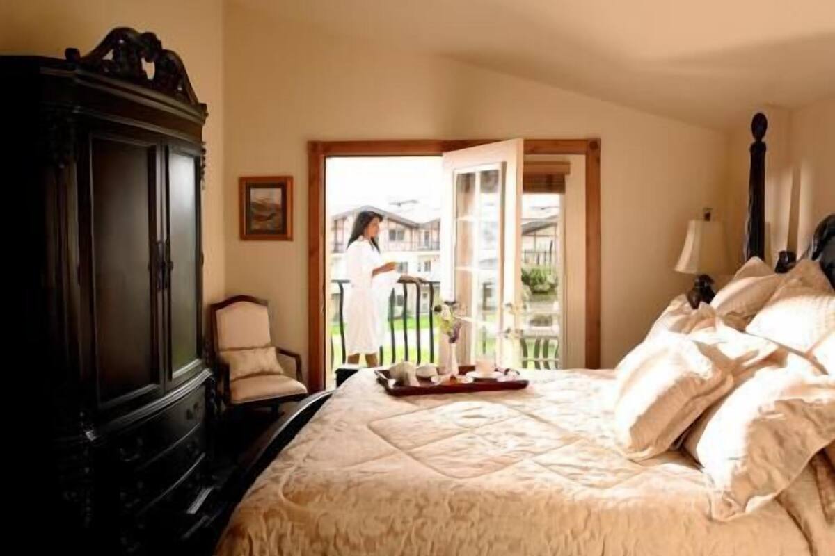 A bedroom with a large bed, a wooden wardrobe, a chair, and a balcony with a view.