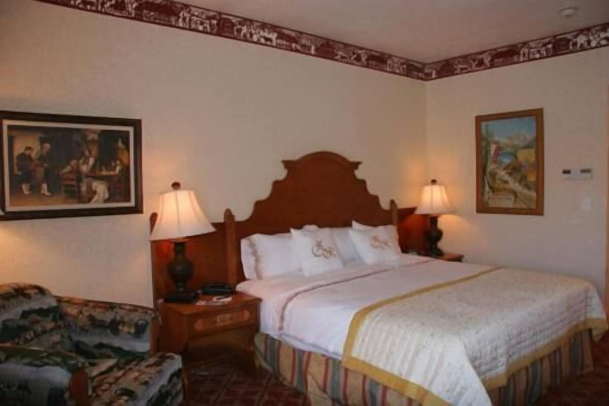 A hotel room with a bed, two bedside lamps, a nightstand, a chair, and two framed pictures on the walls.