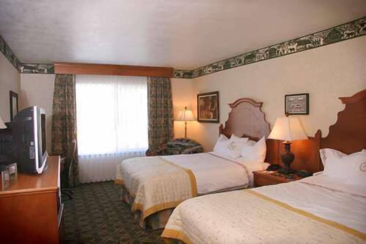 A hotel room with two beds, a television, and a window with curtains.
