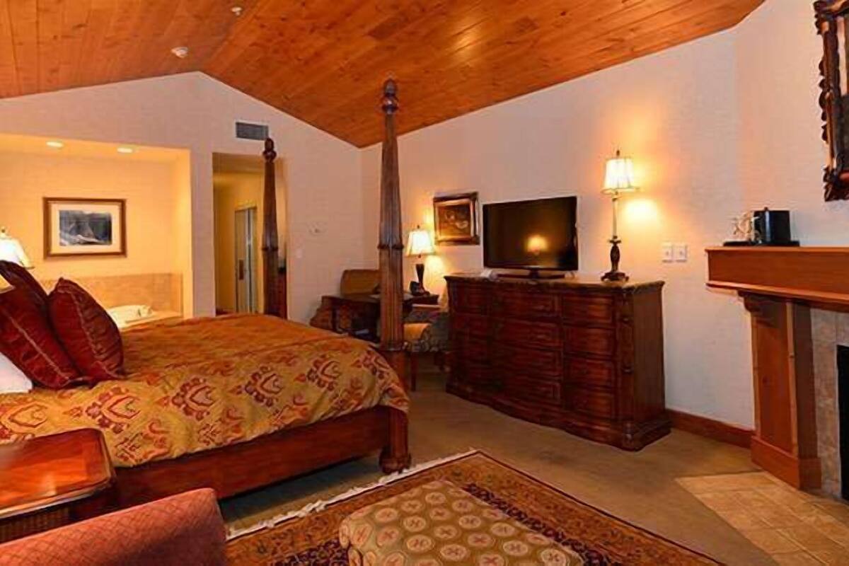 A bedroom with a large bed, wooden dresser, television, and fireplace.