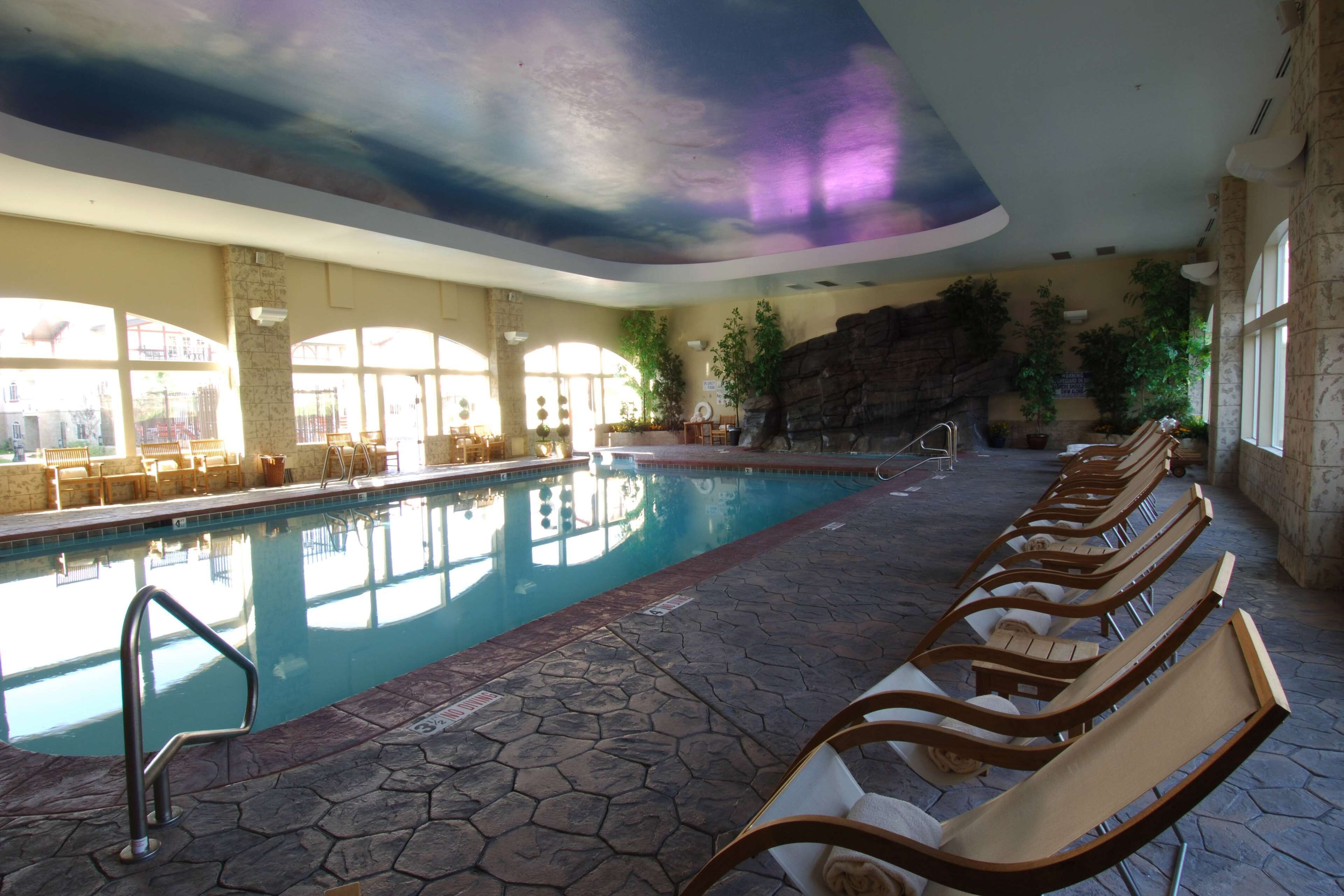 An indoor swimming pool with lounge chairs and a stone-tiled floor.