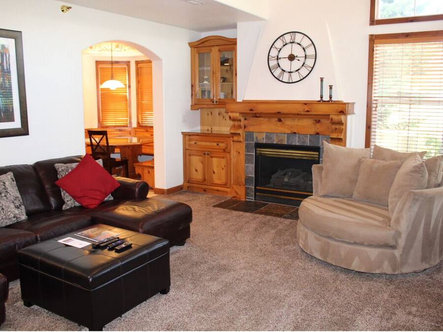 A living room with a fireplace, a clock, and a dining area with wooden cabinets.
