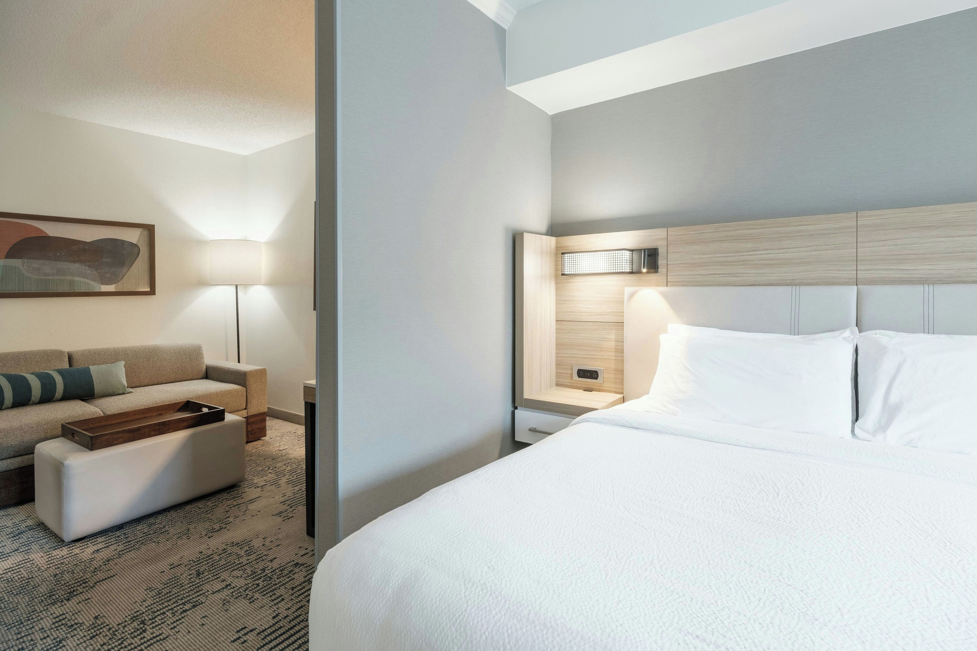 Ein modernes Hotelzimmer mit einem großen Bett, einer Couch, einem kleinen Tisch und einem Nachttisch mit Lampe.