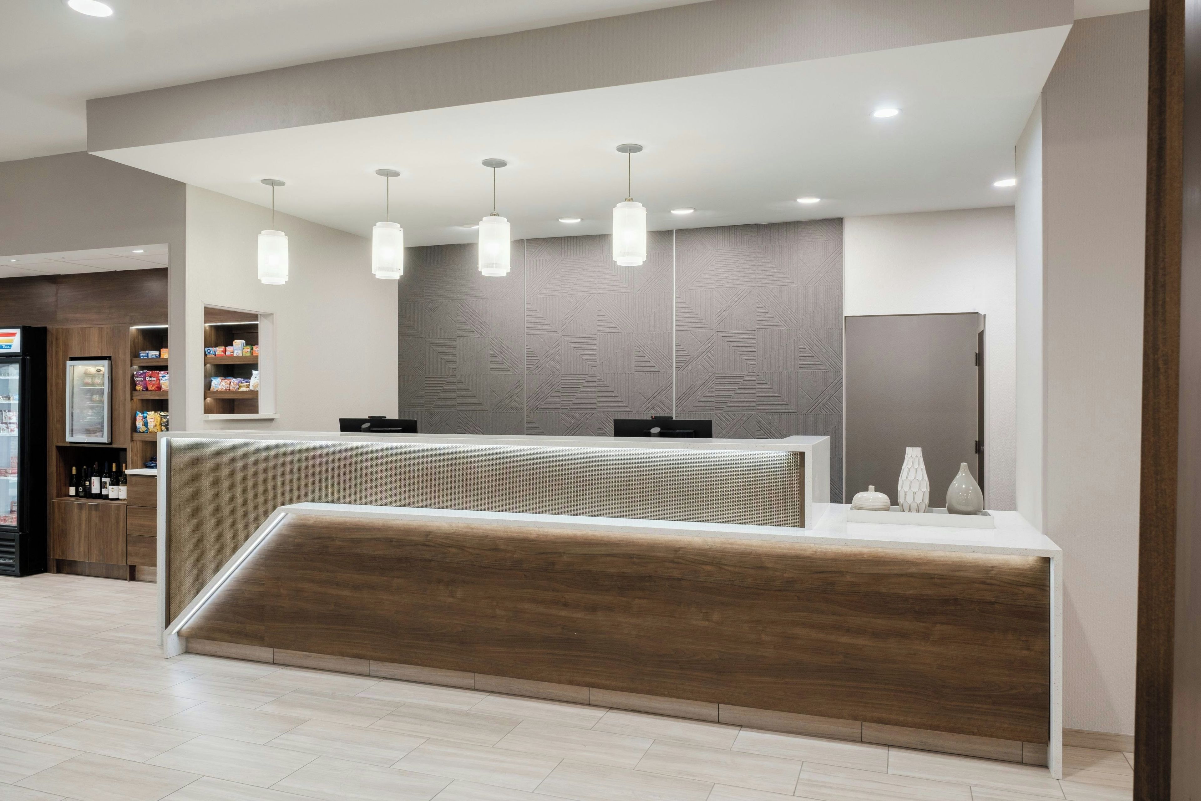 Un área de recepción con un mostrador de madera, iluminación colgante y un revestimiento de pared con diseño.