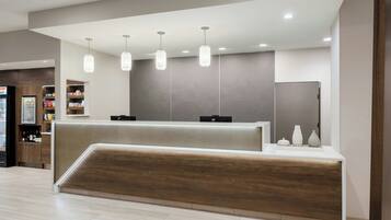 Un área de recepción con un mostrador de madera, iluminación colgante y un revestimiento de pared con diseño.