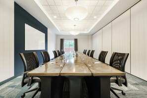 A conference room with a long table, chairs, a projector screen, and a view of the outdoors.