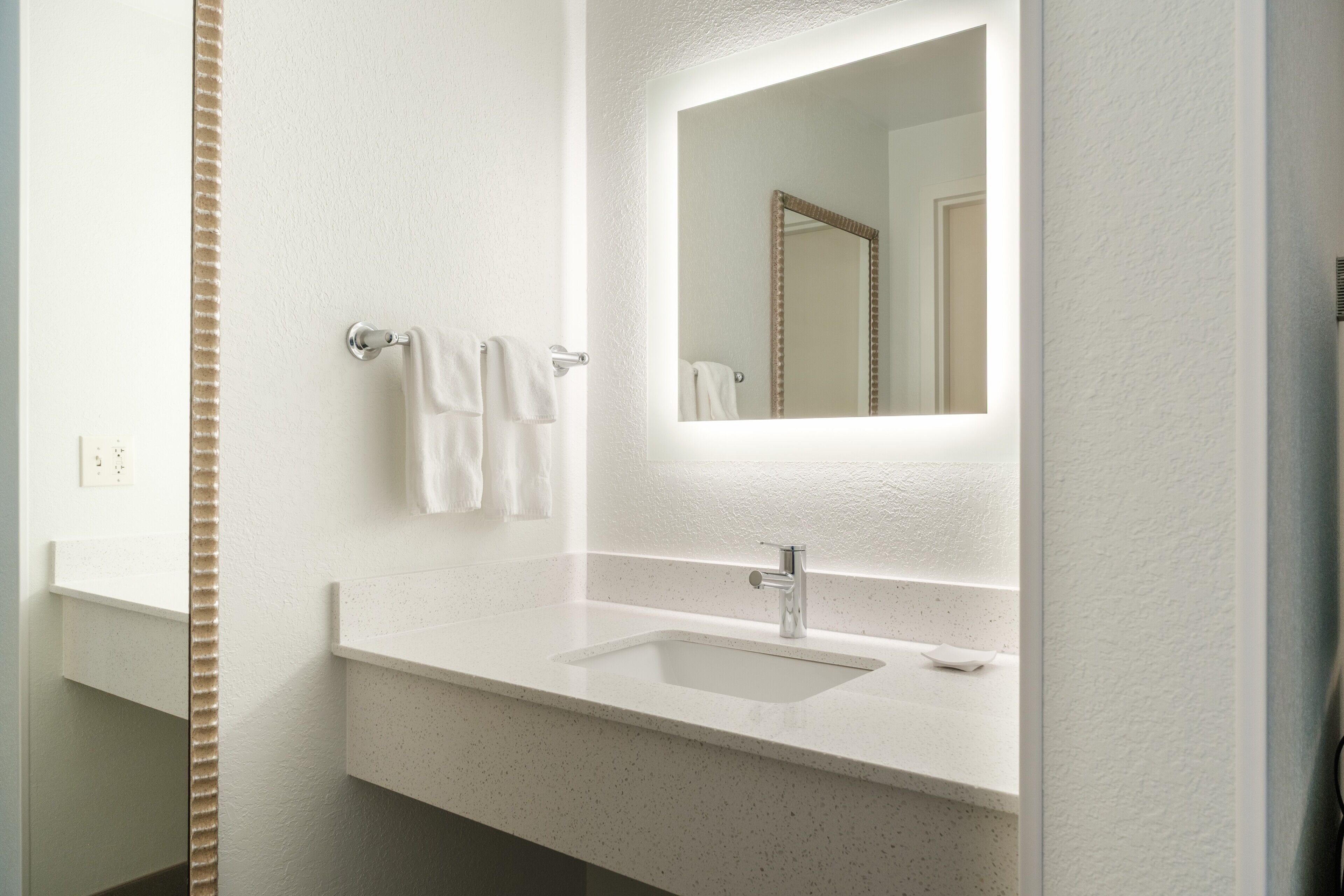 A bathroom with a white sink, a mirror, and two towels hanging on a towel rack.