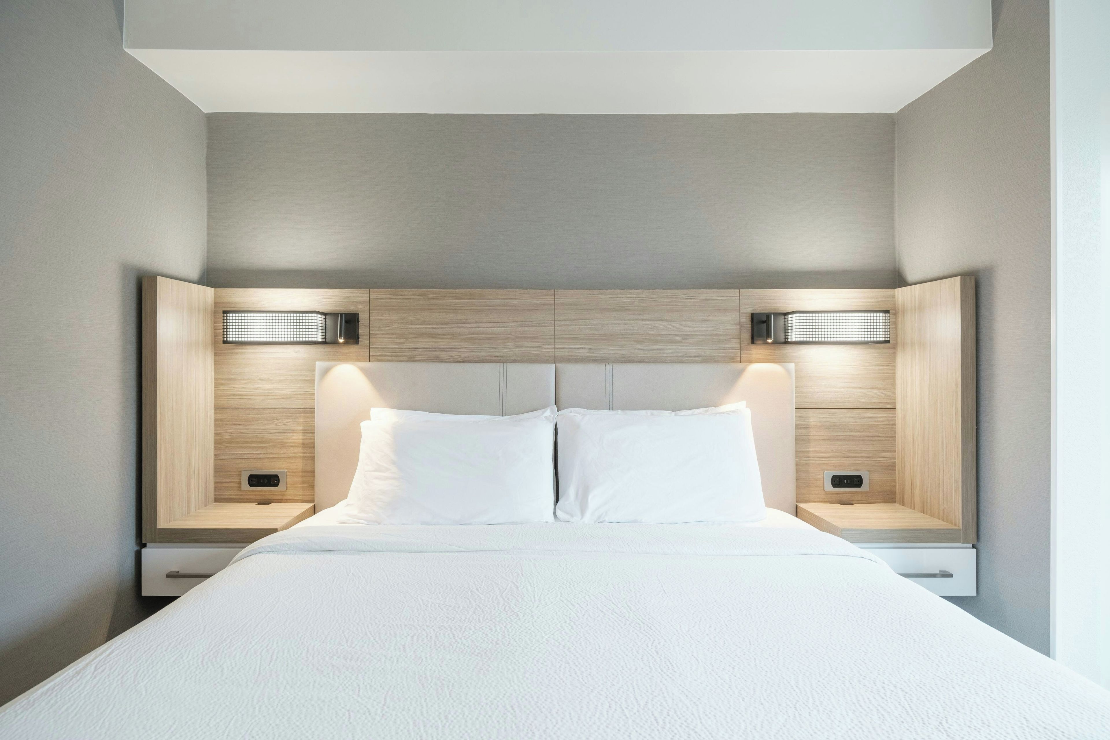 Quarto de hotel moderno com uma cama grande, duas mesas de cabeceira e cabeceira com iluminação embutida.