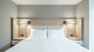 Quarto de hotel moderno com uma cama grande, duas mesas de cabeceira e cabeceira com iluminação embutida.