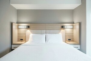 Quarto de hotel moderno com uma cama grande, duas mesas de cabeceira e cabeceira com iluminação embutida.
