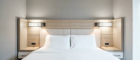 A modern bedroom with a large bed, two bedside tables, and a headboard with integrated lighting.