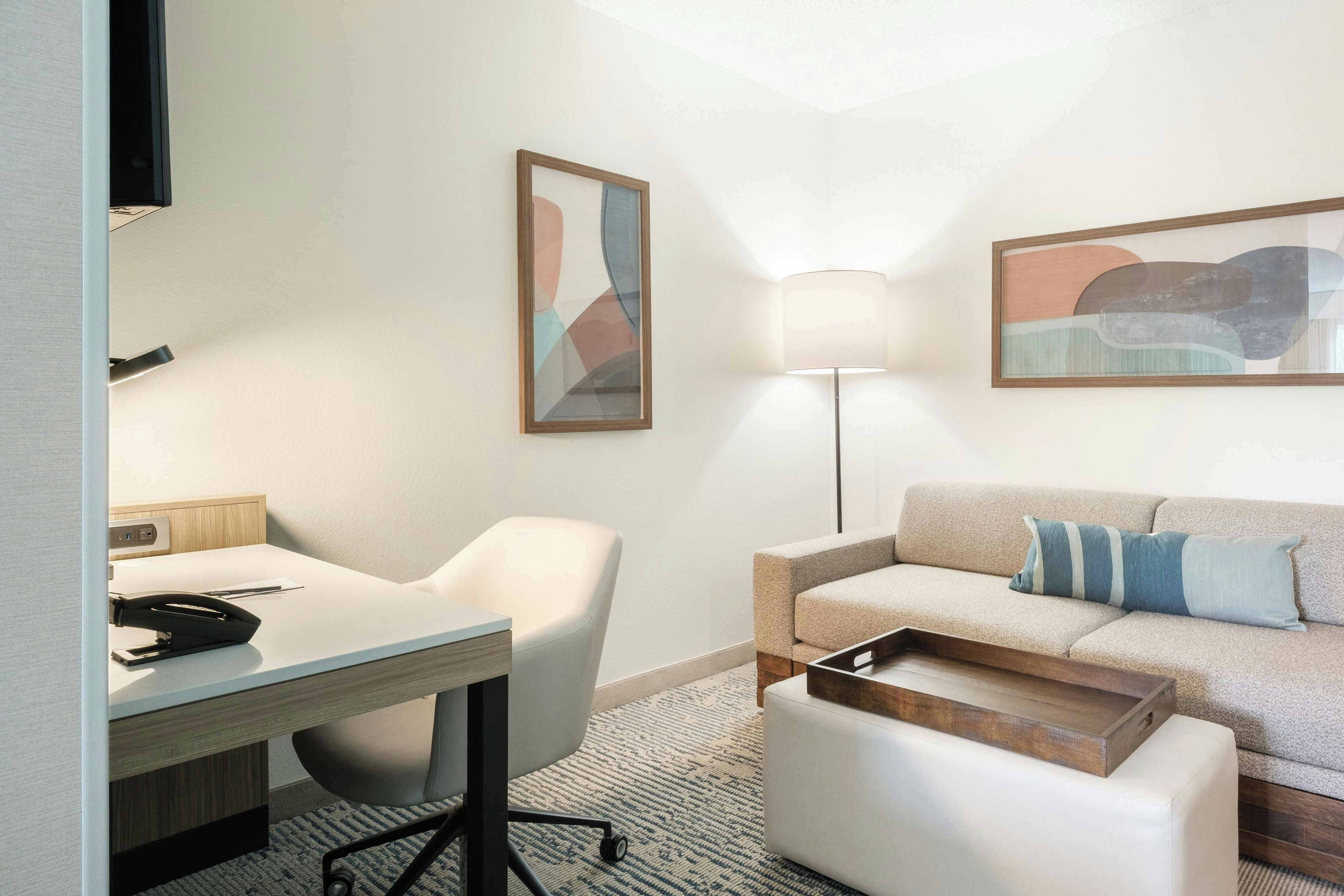 Una habitación de hotel moderna con escritorio, silla, sofá y lámpara.