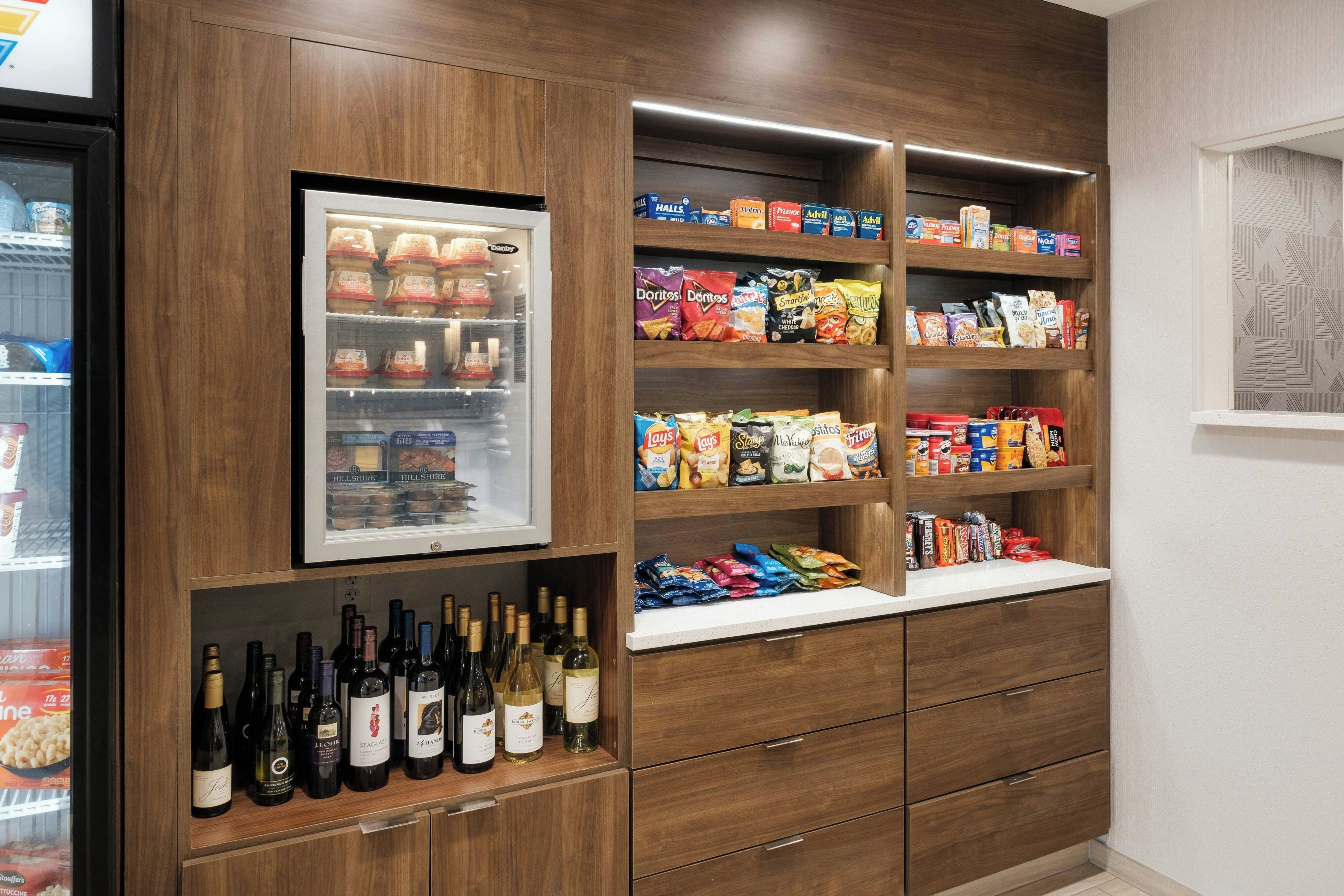 Un depósito con estanterías que contienen aperitivos, una sección refrigerada con productos lácteos y una repisa inferior con botellas de vino.