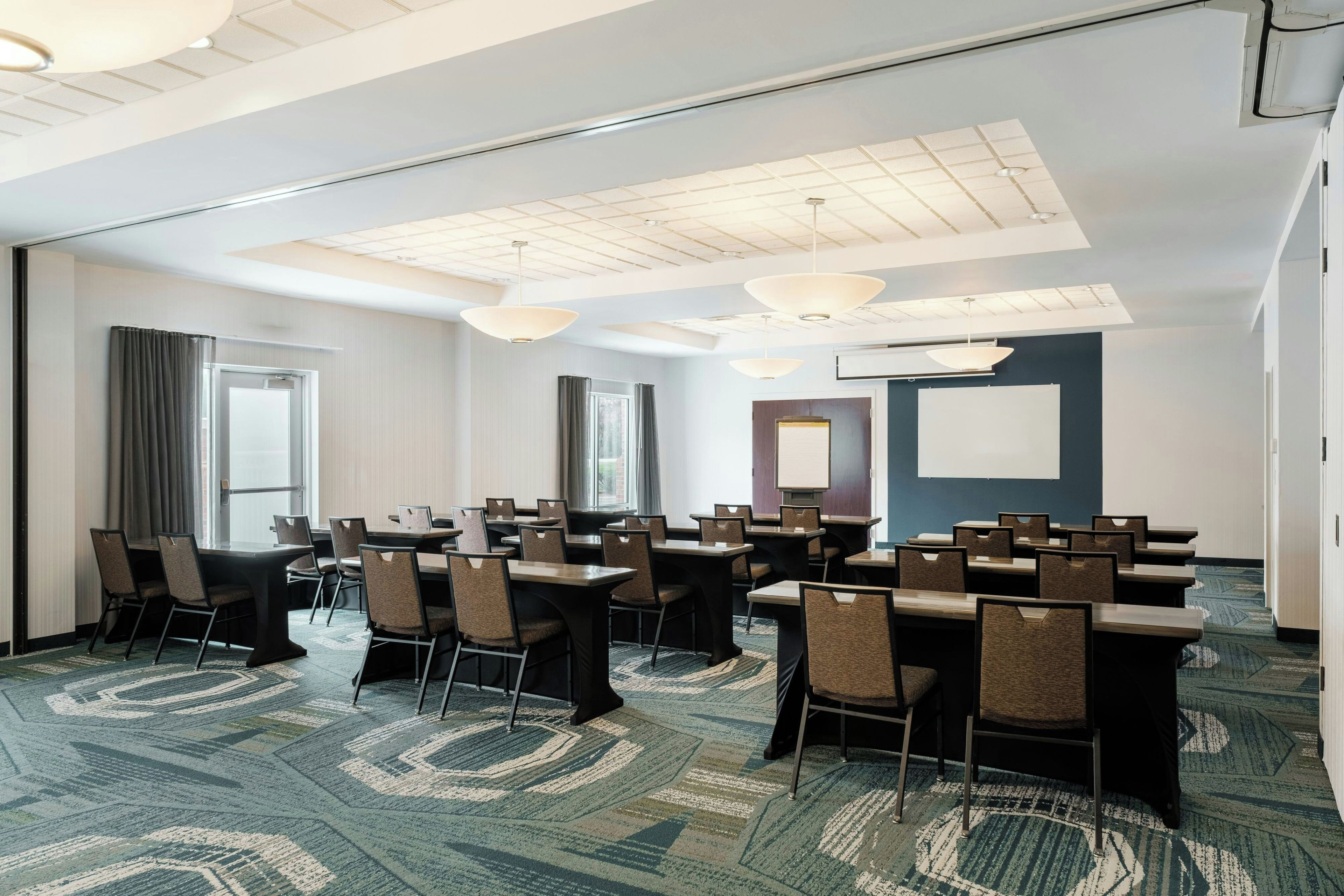 A conference room with tables and chairs, a whiteboard, and a projector screen.