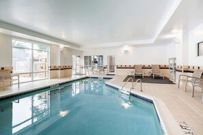 Ein Schwimmbecken mit klarem, blauem Wasser, umgeben von Liegestühlen und einem sonnendurchfluteten Raum mit großen Fenstern.