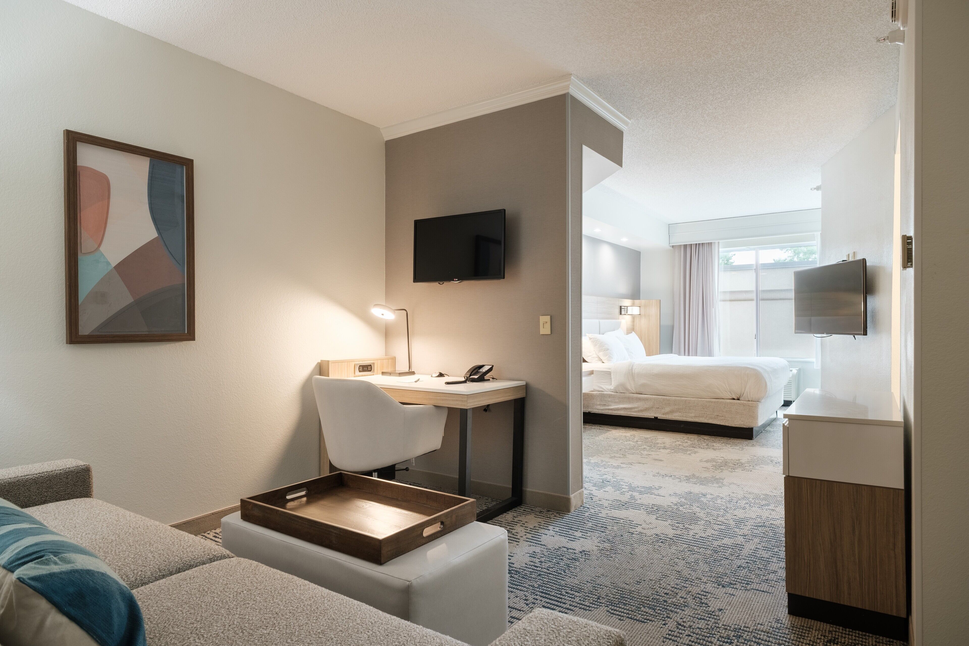 Habitación de hotel con cama, escritorio, silla, televisor y un cuadro en la pared.