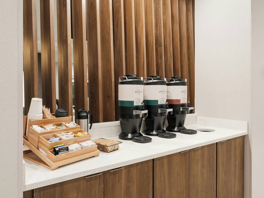 Una estación de café con varios dispensadores, una tetera y una bandeja de vasos desechables.