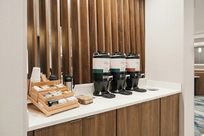 Una estación de café con varios dispensadores, una tetera y una bandeja de vasos desechables.
