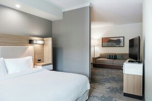 Ein Hotelzimmer mit Bett, Schreibtisch, Sessel, Fernseher und einem Bild an der Wand.