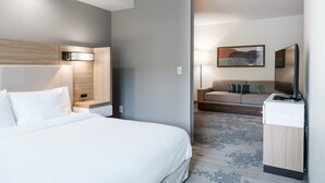 A hotel room with a bed, a desk, a chair, a sofa, and a painting on the wall.