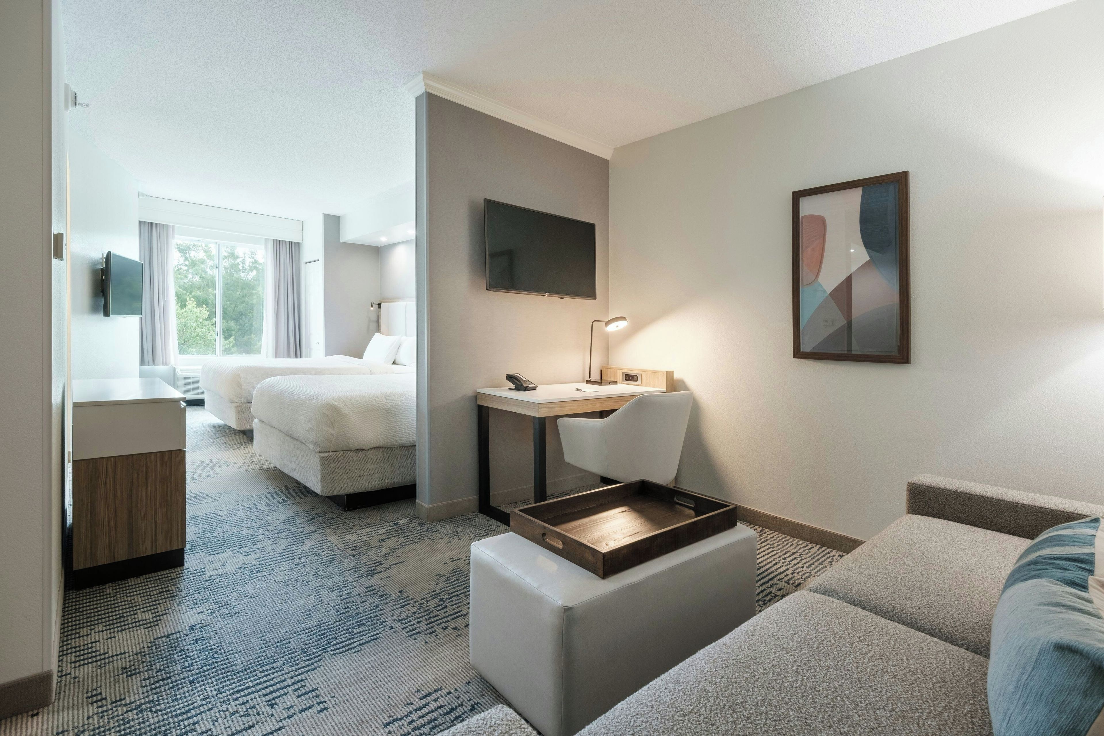 Une chambre d’hôtel avec un lit, un bureau, une chaise, une télévision et un tableau.
