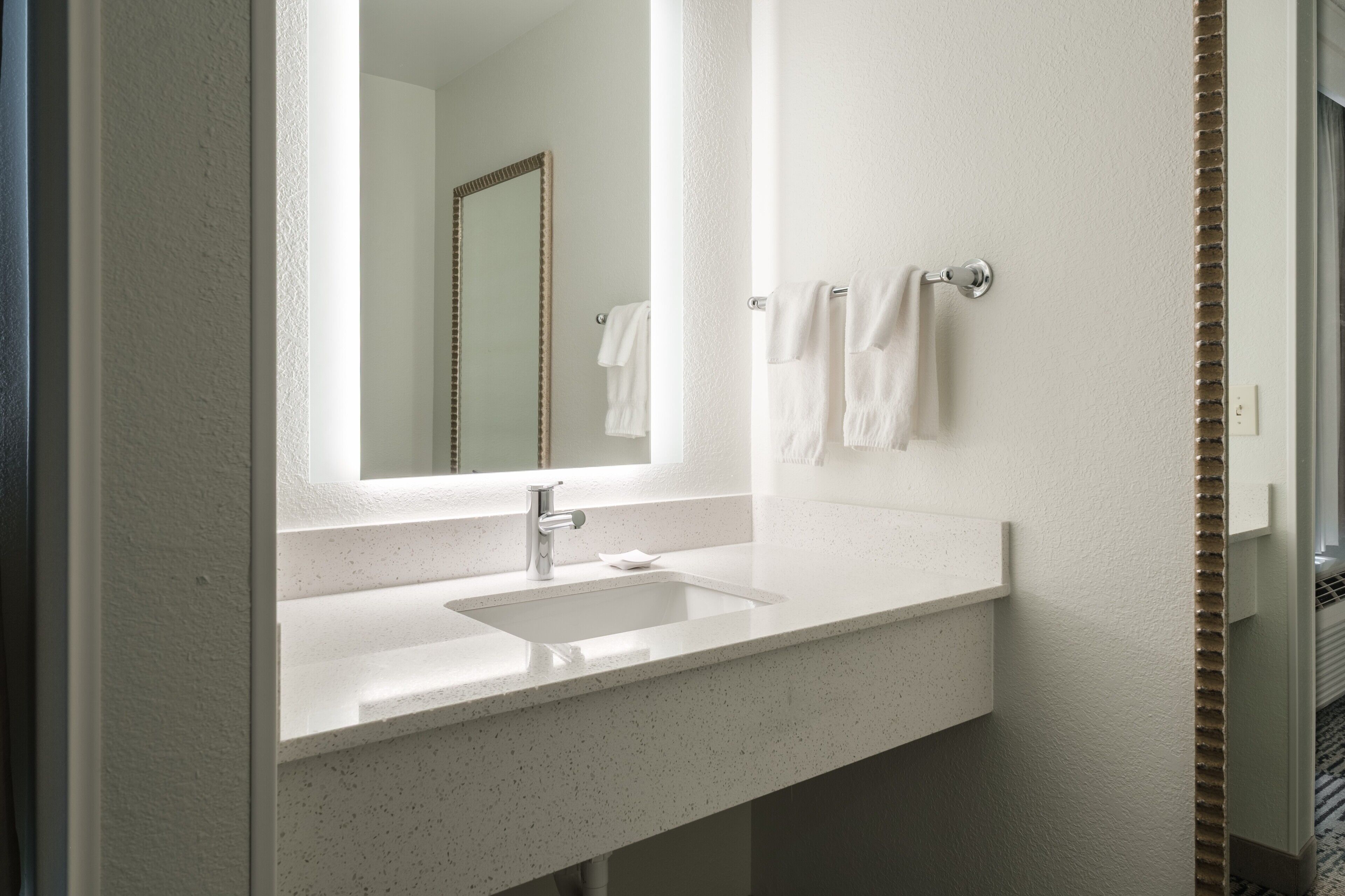 A bathroom with a white sink, a mirror, and two towels hanging on a towel rack.