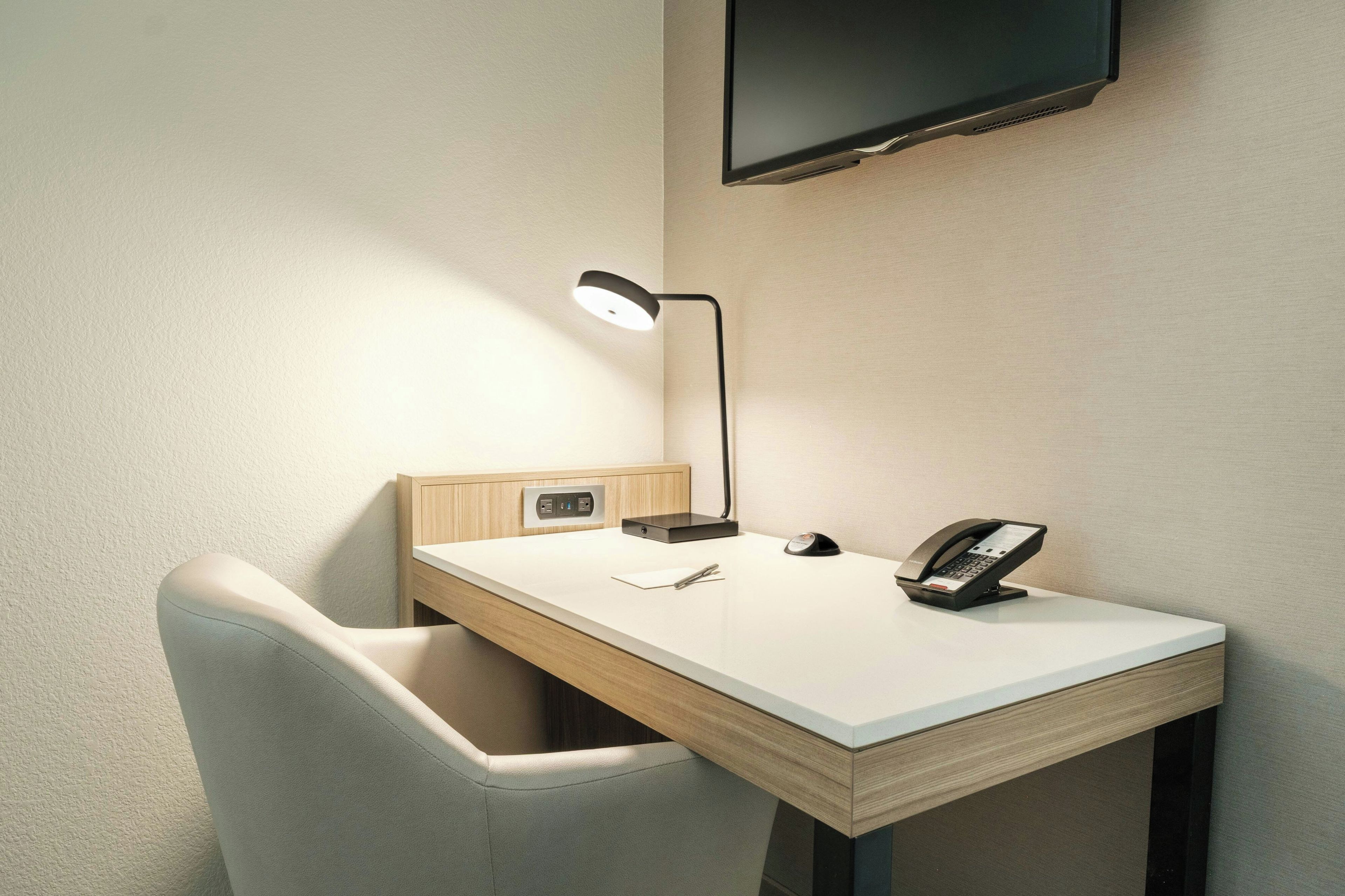 A small, modern desk with a lamp, a telephone, and a power outlet.