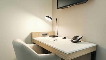 A small, modern desk with a lamp, a telephone, and a power outlet.