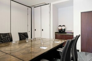 Una sala de conferencias con una mesa larga, sillas, una estación de café y una puerta.