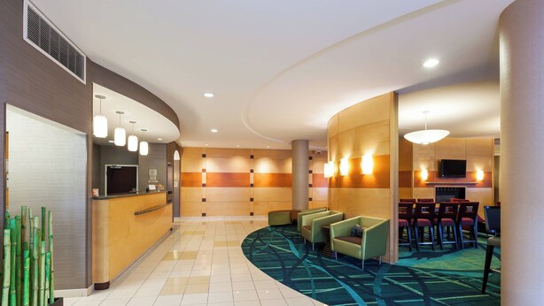 A hotel lobby with a reception desk, seating area, and a television screen.