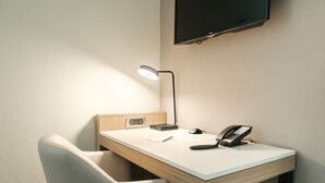 Ein kleiner Schreibtisch mit einer Lampe, einem Telefon und einem an der Wand befestigten Flachbildfernseher.