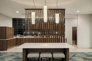 Uma cozinha moderna com ilha central, banquetas, iluminação pendente e divisória de madeira.