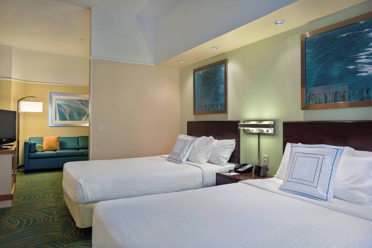 Habitación de hotel con dos camas, un sofá, un escritorio y un cuadro en la pared.