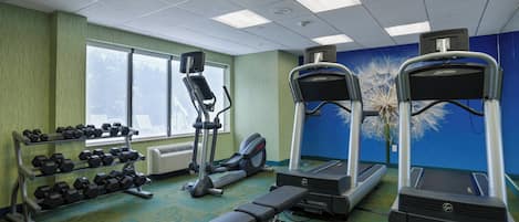 Un gimnasio con cintas de correr, elípticas y una banca.