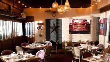 Interior de restaurante con paneles de madera, lámparas colgantes y un menú en la pizarra. Las mesas están dispuestas con vajilla y las sillas están tapizadas.