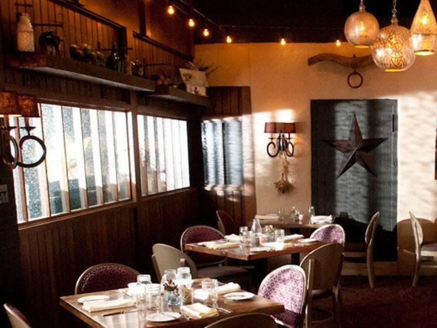 Interior de restaurante con paneles de madera, lámparas colgantes y un menú en la pizarra. Las mesas están dispuestas con vajilla y las sillas están tapizadas.