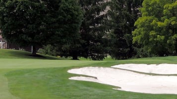 Un parcours de golf avec des bunkers, un espace de repos couvert et un bâtiment avec un toit rouge en arrière-plan.