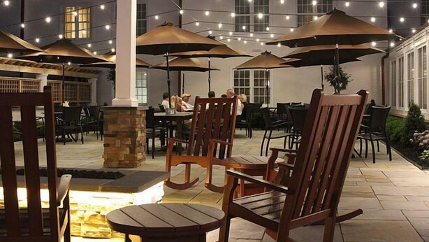 Un espace extérieur aménagé en terrasse, avec des chaises et des tables en bois, des guirlandes lumineuses et des parasols.