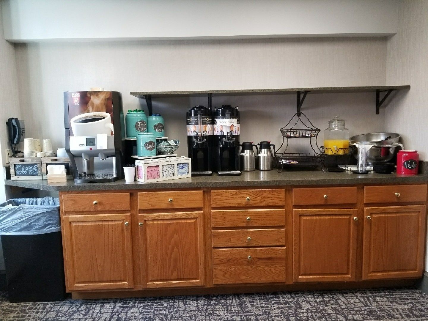 A kitchen with a coffee maker, tea kettles, and a fruit basket on the counter.