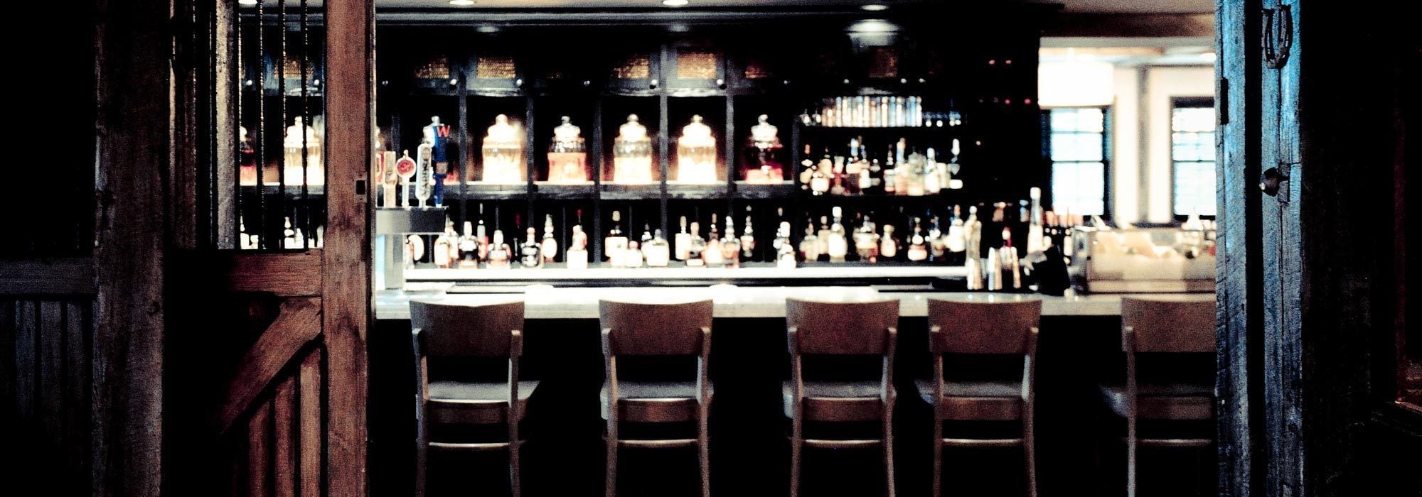 Una zona de bar con sillas de madera y estanterías llenas de botellas.