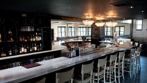 Un espace bar moderne doté d’un long comptoir, de tabourets et d’une variété de bouteilles et de verres.