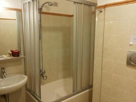 Baño con ducha envuelta en vidrio, lavamanos y retrete.