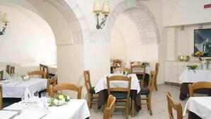 Um restaurante com mesas preparadas para refeições, cadeiras de madeira e toalhas de mesa brancas.