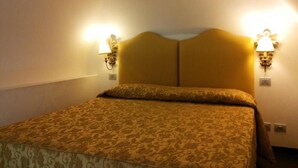 Quarto de hotel com cama de casal, duas luminárias na parede e colcha estampada.